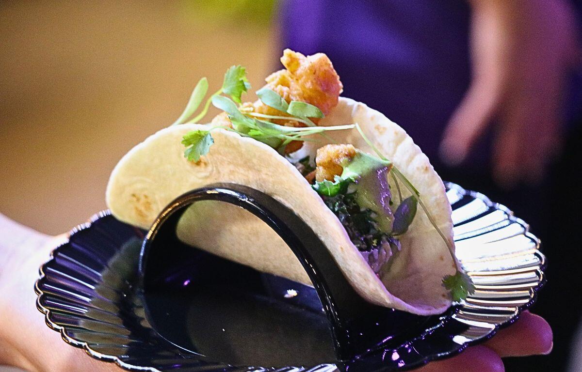 A taco featuring meat, sauce and vegetables sits on a black plate.