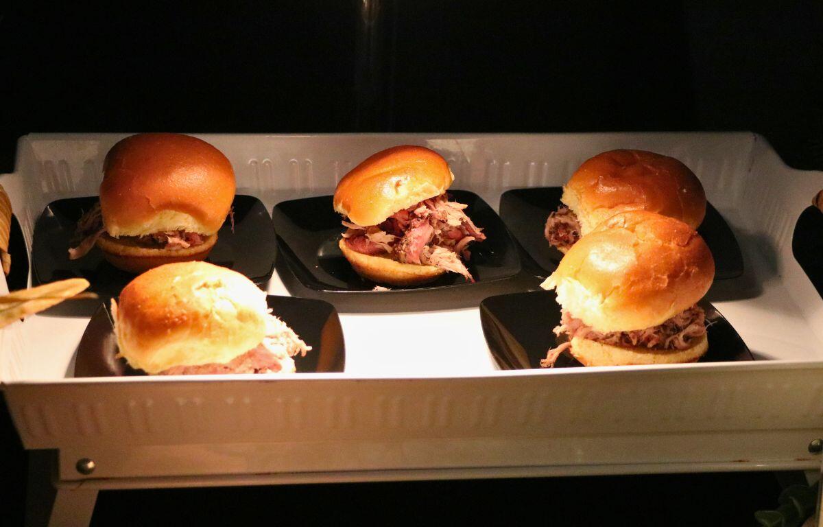 Pulled pork sandwiches on small black plates sit under a warmer.