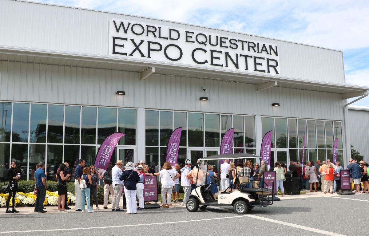 The World Equestrian Center Expo Center facade with purple feather flags advertising the Ocala Food and Wine Festival. Attendees await entry.