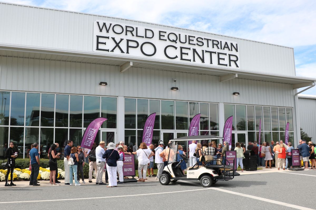 The World Equestrian Center Expo Center facade with purple feather flags advertising the Ocala Food and Wine Festival. Attendees await entry.
