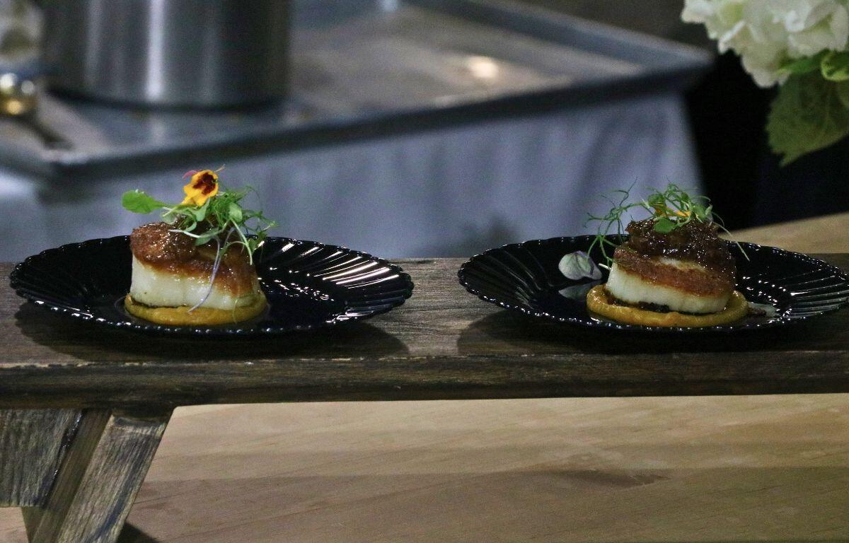 Two black plates contain samples of food on bread with garnish.