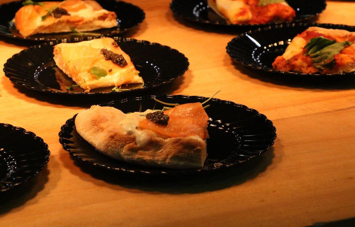 Multiple plated food samples sit on black plates on top of a wooden counter under a bright light.