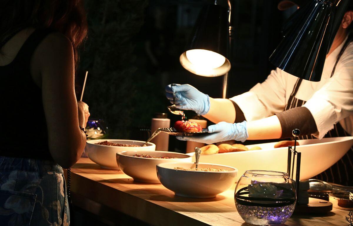 A worker wearing blue gloves frosts a donut on a black plate for a customer.