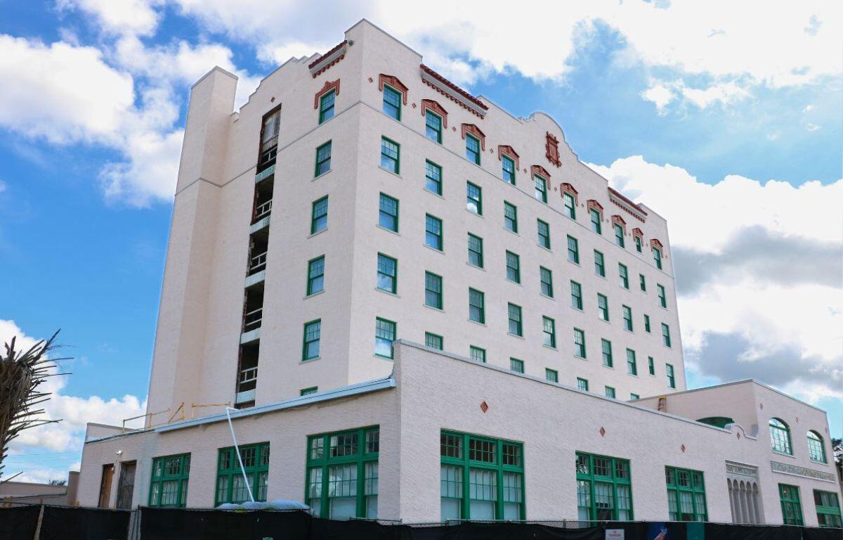Blue and white sky in the background. Tall building, with windows with ornamental palm and a construction fence in the foreground.