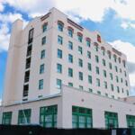 Blue and white sky in the background. Tall building, with windows with ornamental palm and a construction fence in the foreground.
