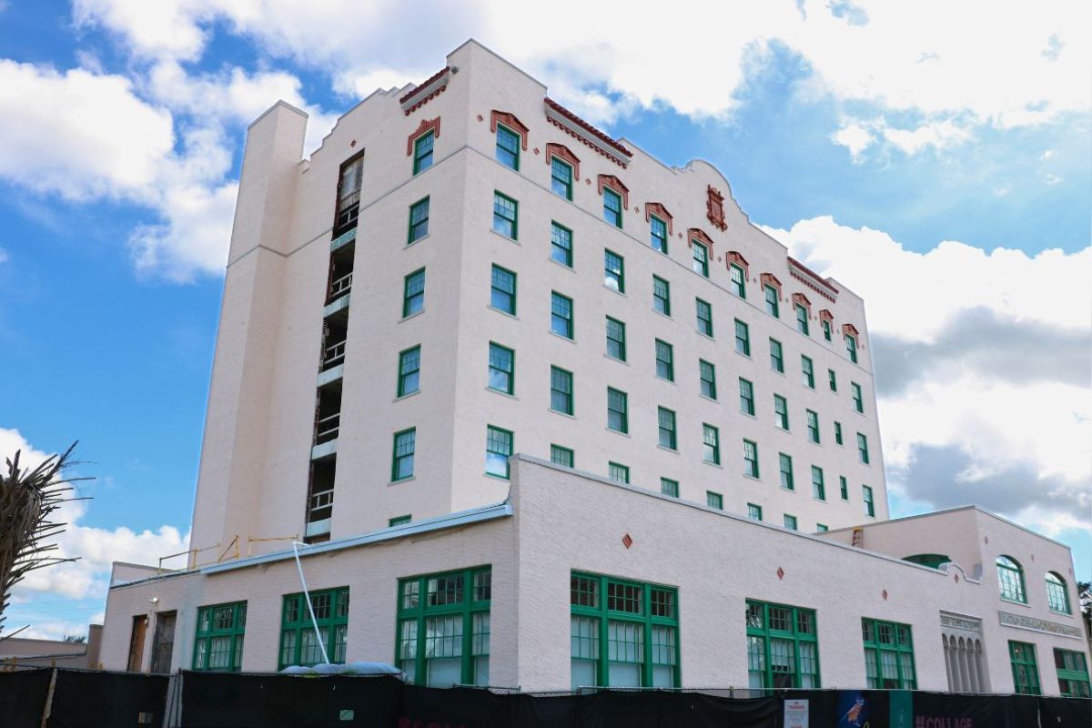 Blue and white sky in the background. Tall building, with windows with ornamental palm and a construction fence in the foreground.