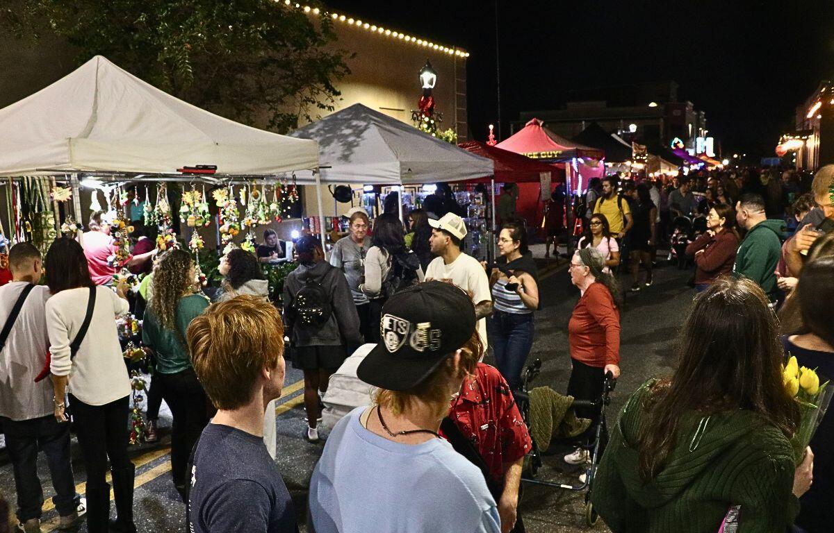 A crowd of people walk on a dimly lit street with canopies lining on side.