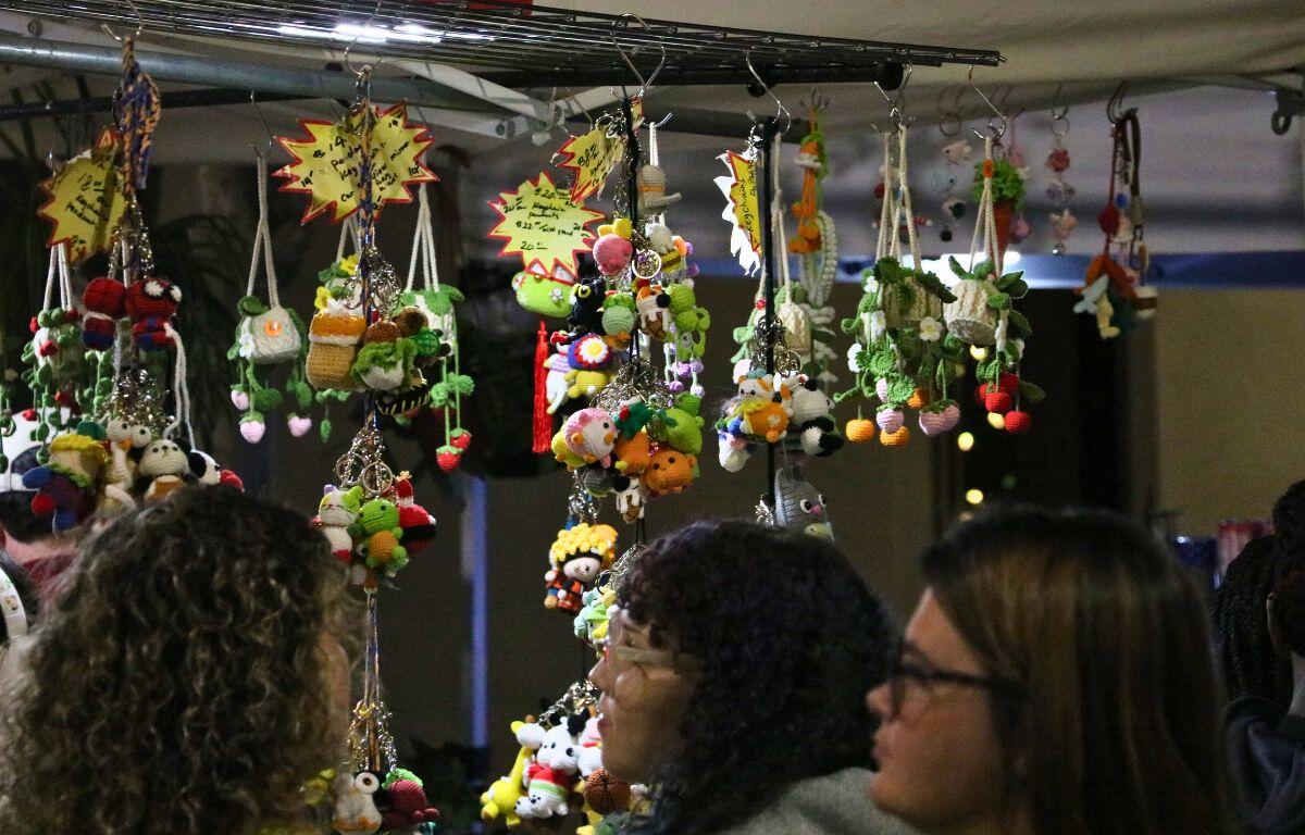 A vendor booth displays tiny crochet keychains from a suspending rack as a group of customers look through the merchandise.