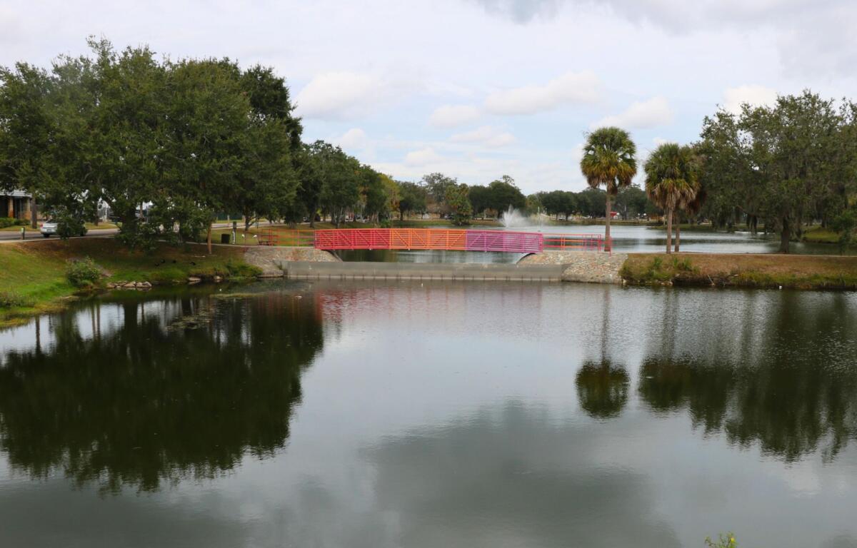 Lake Tuscawilla with trees and grass surrounding it, a bridge going over it and a fountain spraying upward behind it.