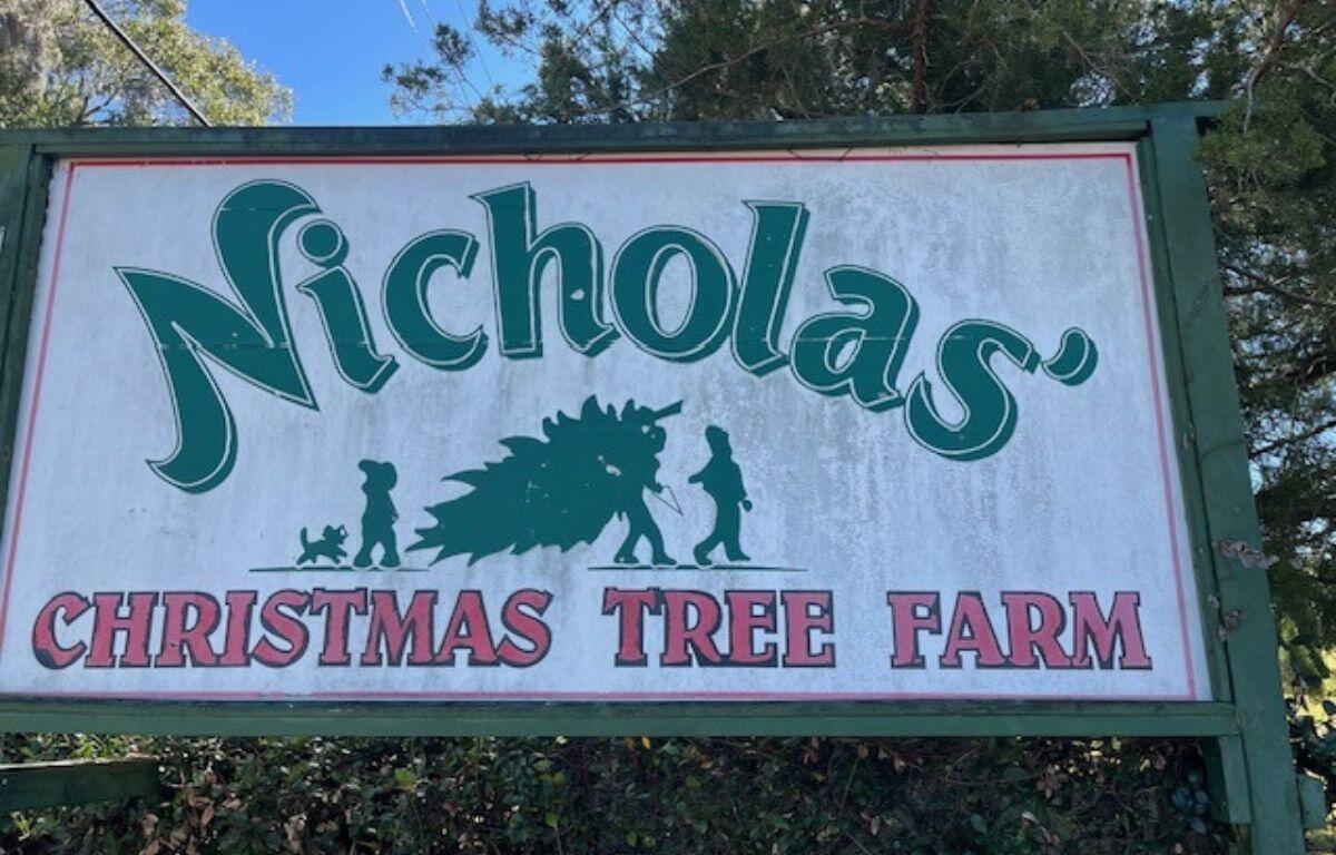 A sign with lettering of different fonts and sizes, with an image, with a tree line in the background.