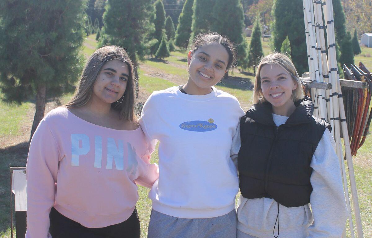 A tree to the left of a family, with one daughter to the left of the two parents who are holding a child and another daughter to the right, who are standing on grass with trees in the background.