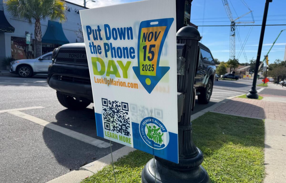 A "Put Down the Phone Day" yard sign placed in the grass in Downtown Ocala. The sign is in front of a parked car and parking meter.
