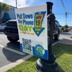 A "Put Down the Phone Day" yard sign placed in the grass in Downtown Ocala. The sign is in front of a parked car and parking meter.