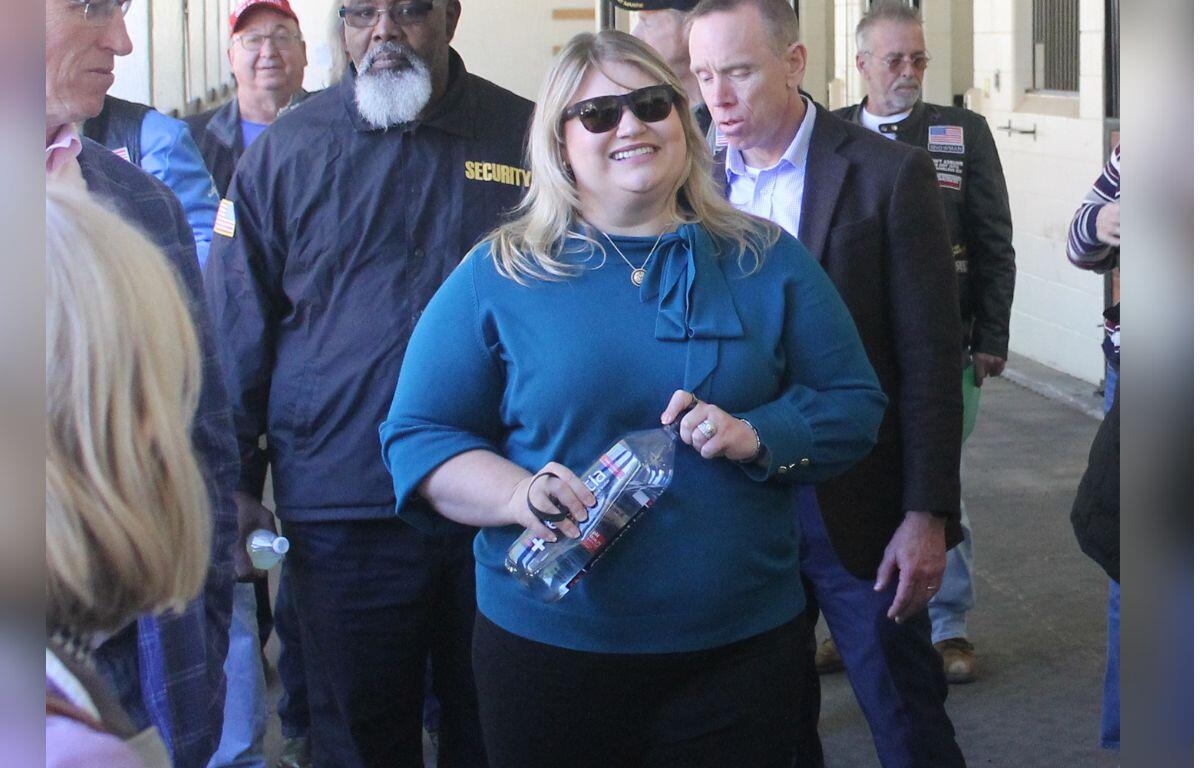 People walking down a shedrow of a barn, with the woman in the center holding a bottle of water.
