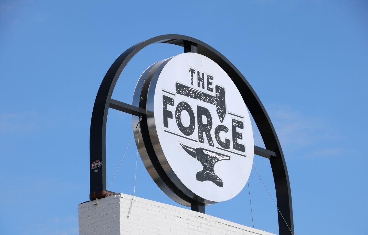 Close-up of The Forge's circular black-and-white sign mounted against a clear blue sky.