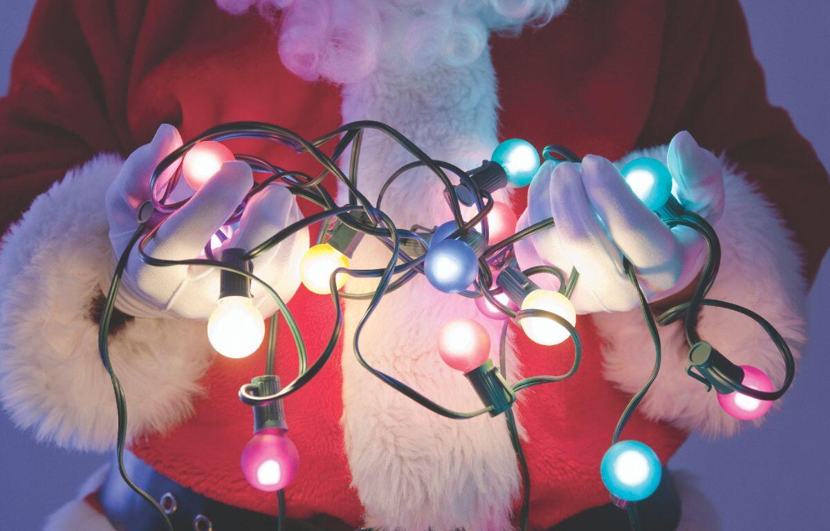 Santa's midsection shown against a light blue backdrop. He is holding lit Christmas lights in his hands.