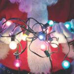 Santa's midsection shown against a light blue backdrop. He is holding lit Christmas lights in his hands.