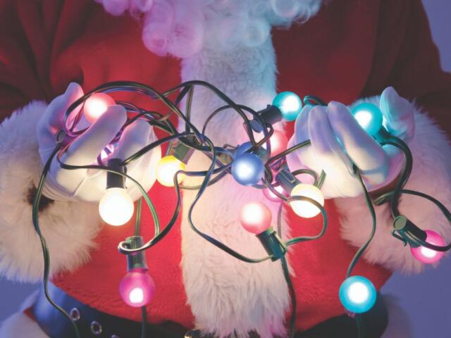 Santa's midsection shown against a light blue backdrop. He is holding lit Christmas lights in his hands.