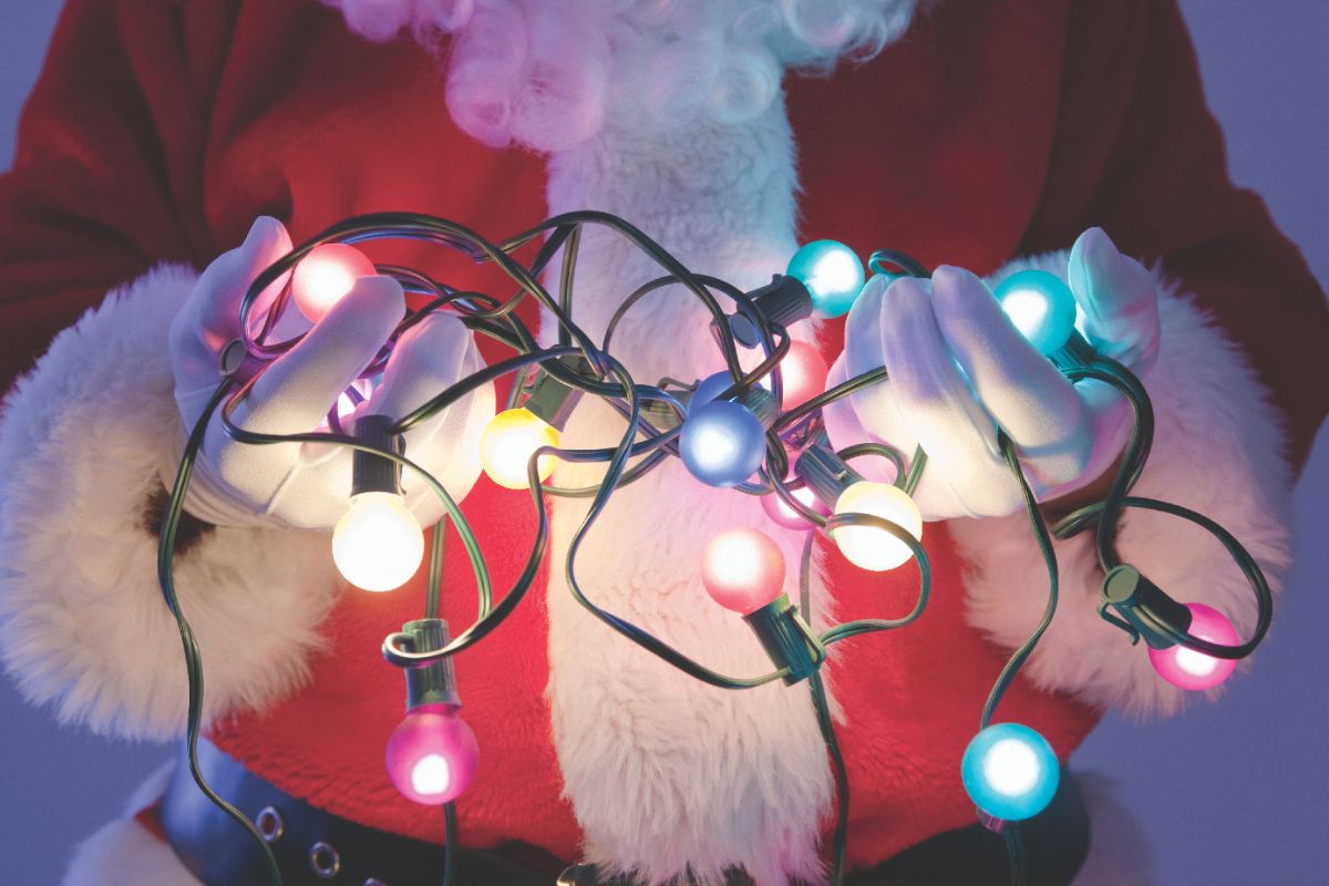 Santa's midsection shown against a light blue backdrop. He is holding lit Christmas lights in his hands.