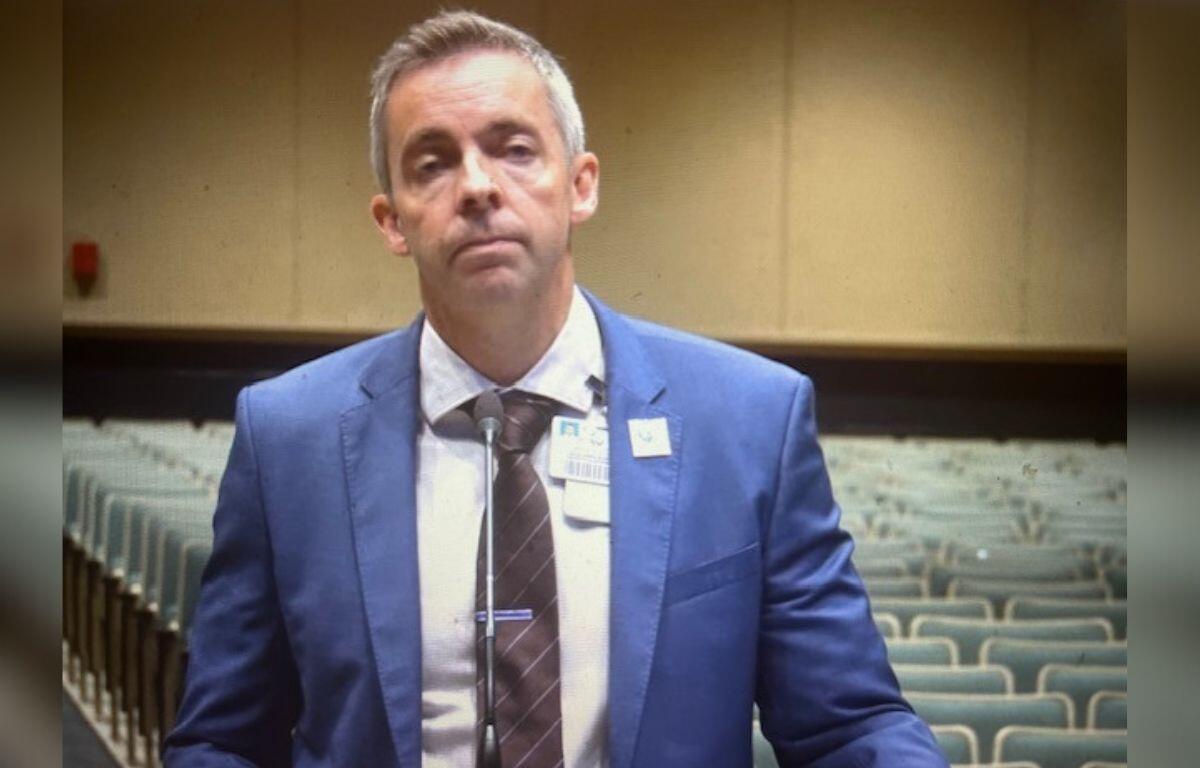 A well-dressed man standing in front of rows of empty seats.