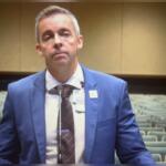 A well-dressed man standing in front of rows of empty seats.