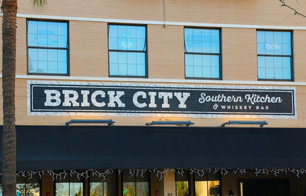 A yellow building has four windows above the entrance. Below the windows is a black and white sign reading, "Brick City Southern Kitchen & Whiskey Bar."