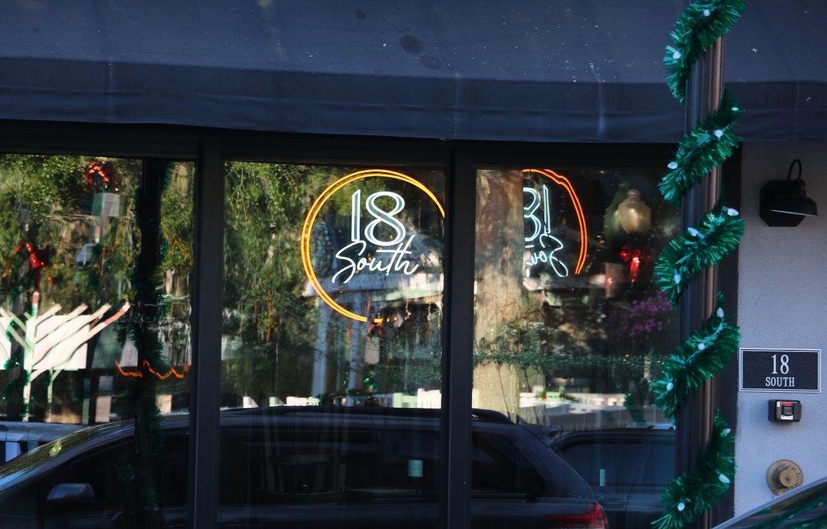 A neon light up sign can be seen through a glass window. The sign reads, "18 South."