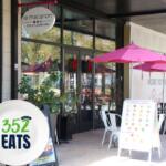 Outdoor seating at Le Macaron French Pastries in Gainesville, with pink umbrellas and a 352 Eats sign near the entrance.