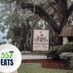 The Braised Onion restaurant sign displayed along a landscaped walkway beneath large, shady trees.