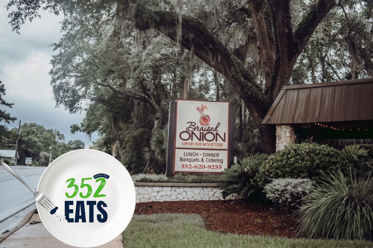 The Braised Onion restaurant sign displayed along a landscaped walkway beneath large, shady trees.