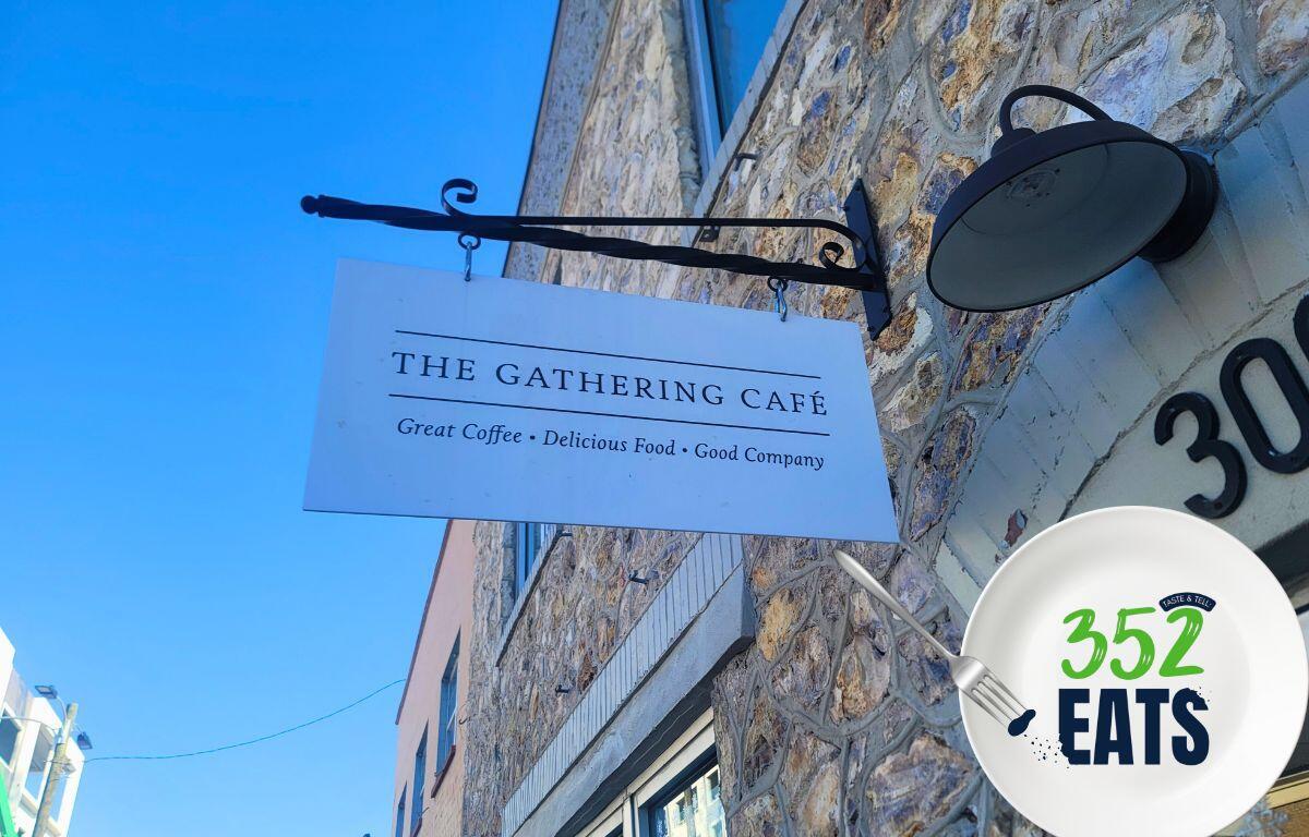 A white sign reading, "The Gathering Cafe" is hung on a historic stone building.