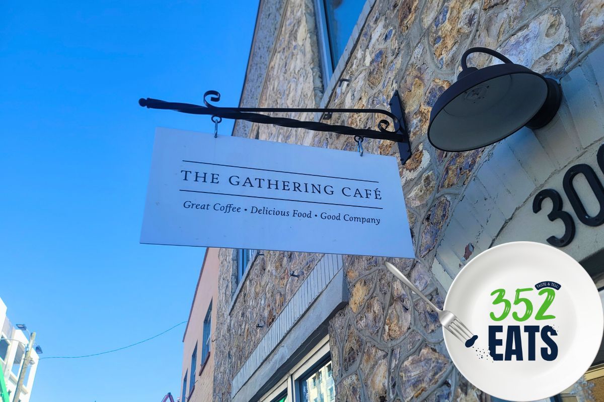 A white sign reading, "The Gathering Cafe" is hung on a historic stone building.