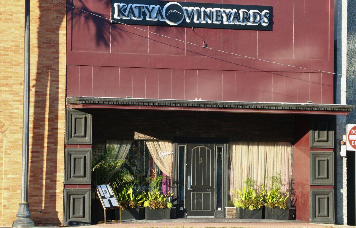 A burgundy building has two windows on the either side of a black door with drawn curtains.