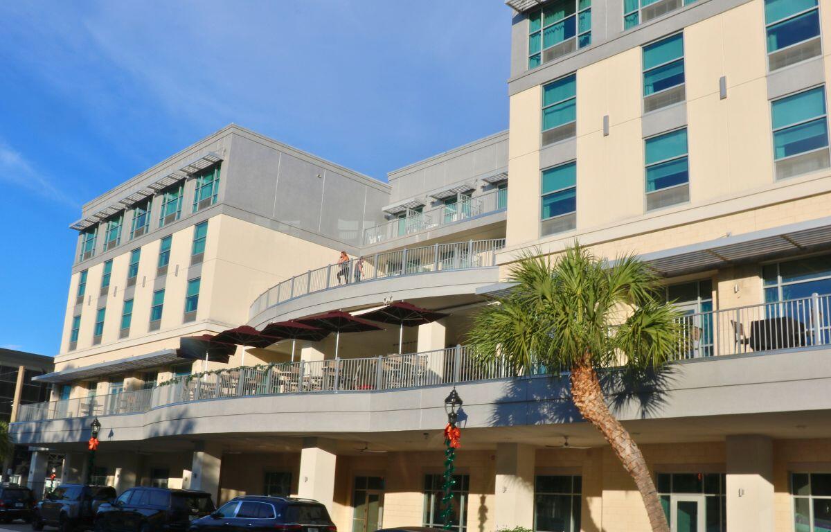 A multistory beige building has two large terraces. The building is on the side of a busy street.