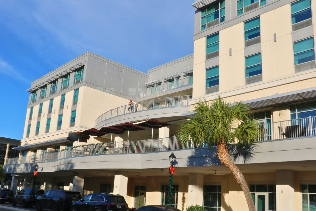A multistory beige building has two large terraces. The building is on the side of a busy street.