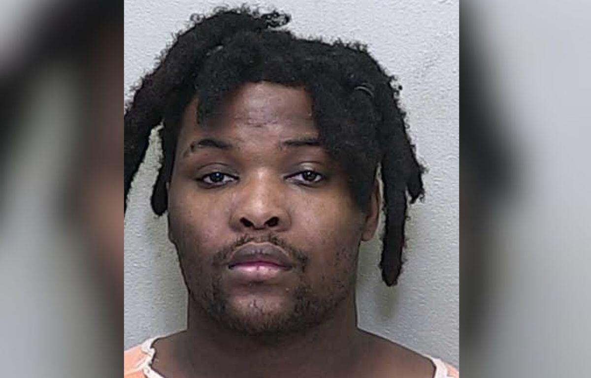 A man in a white and orange jumpsuit standing against a gray wall.