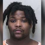 A man in a white and orange jumpsuit standing against a gray wall.