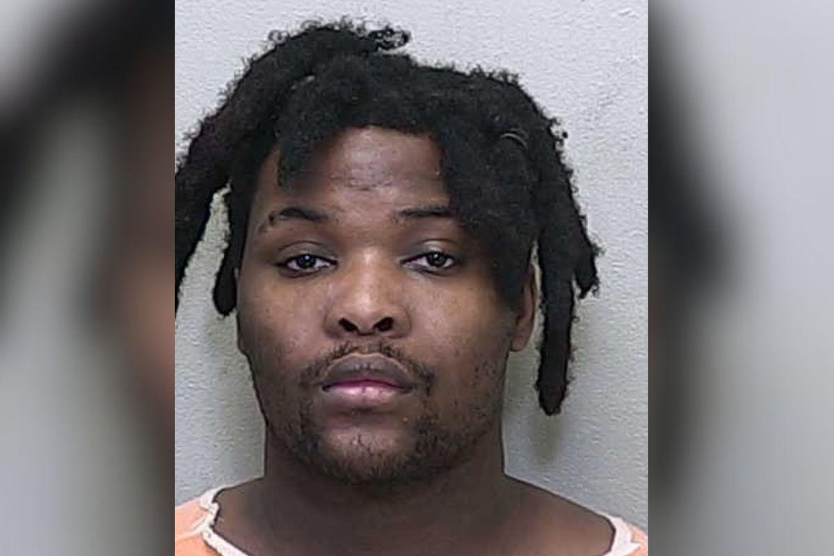 A man in a white and orange jumpsuit standing against a gray wall.