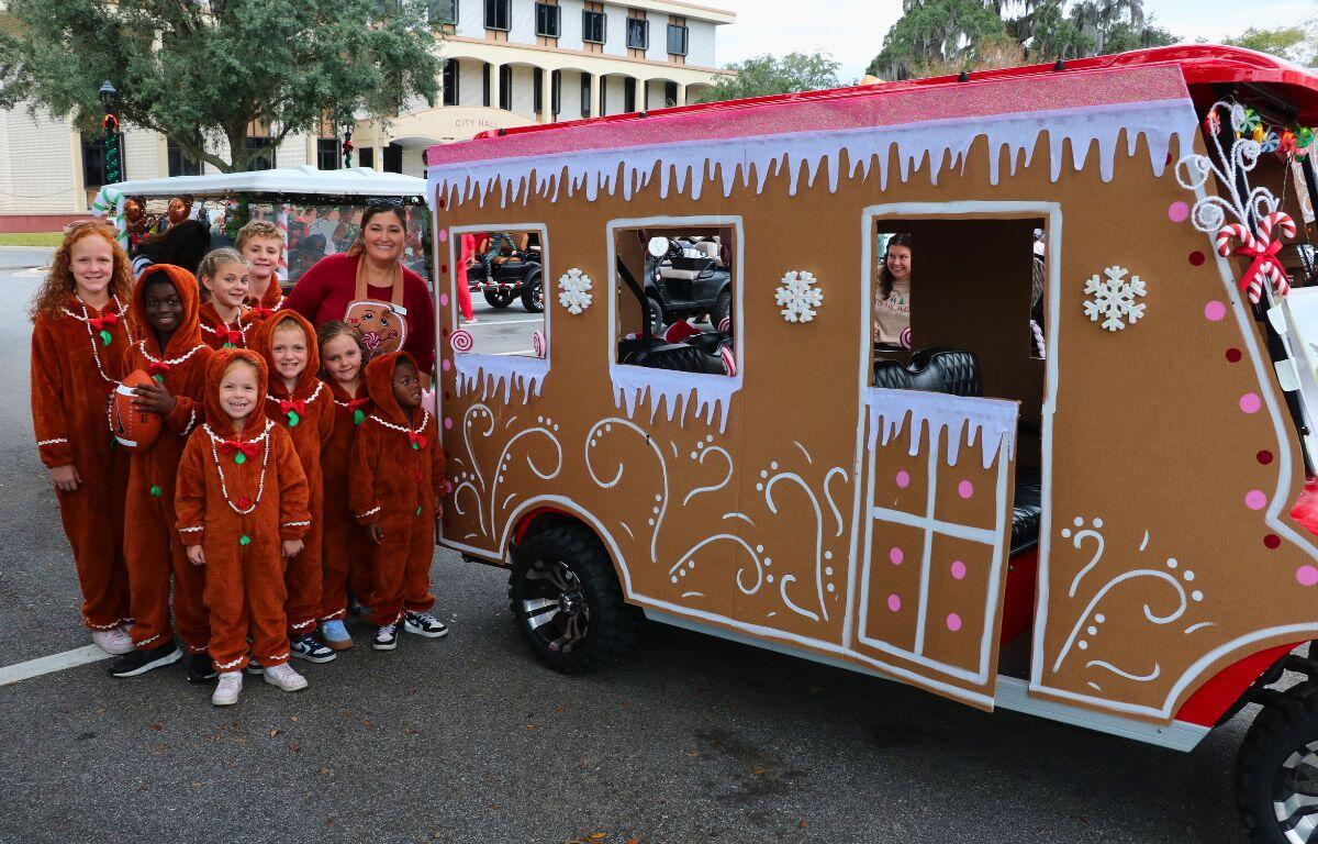 A group of kids pose for a picture next to a golf cart decorated to look like a gingerbread house.