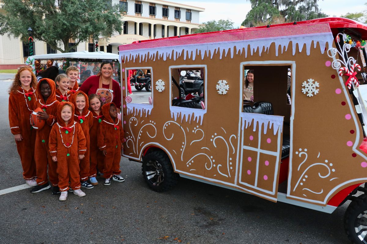 A group of kids pose for a picture next to a golf cart decorated to look like a gingerbread house.