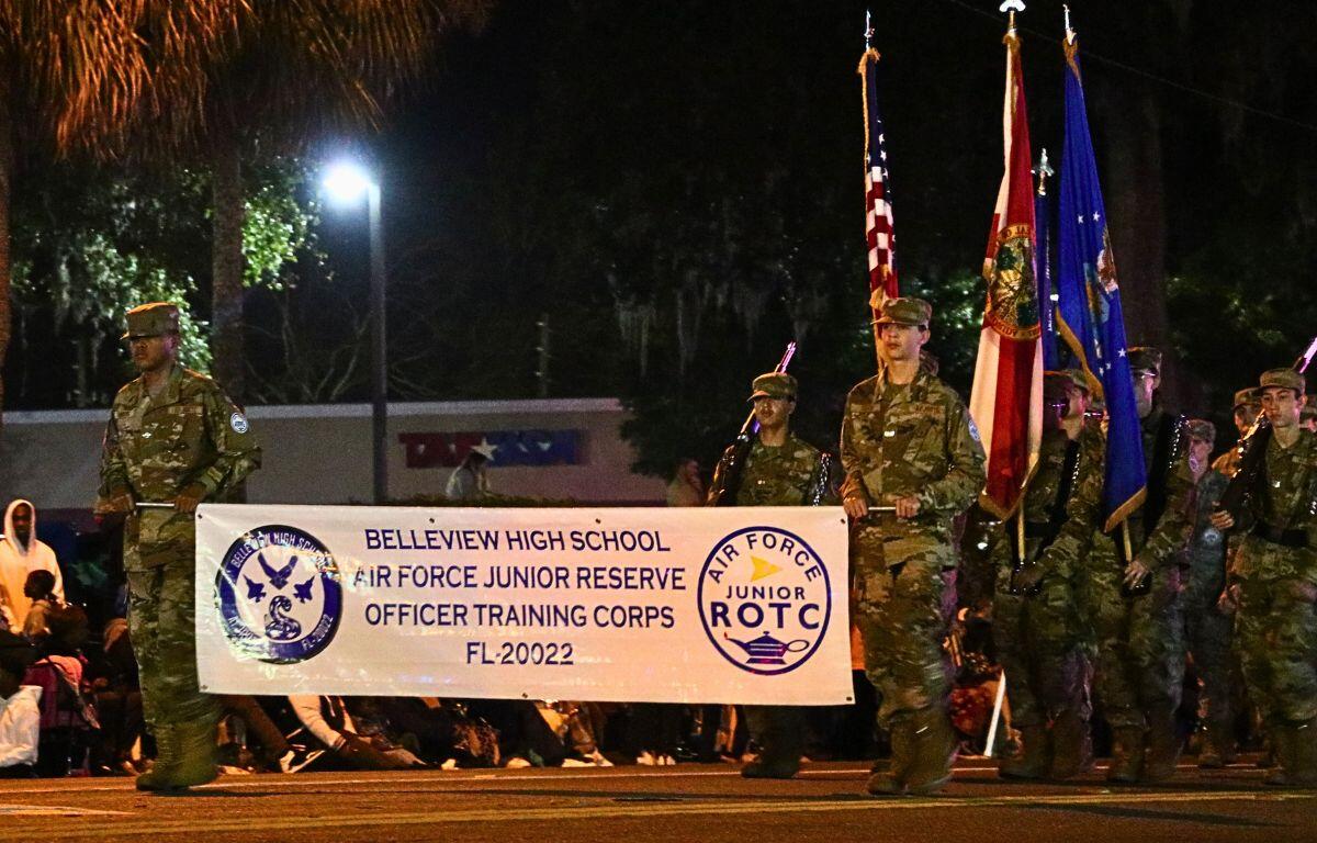 Students in Air Force uniforms march down a dimly lit road holding banners and flags.