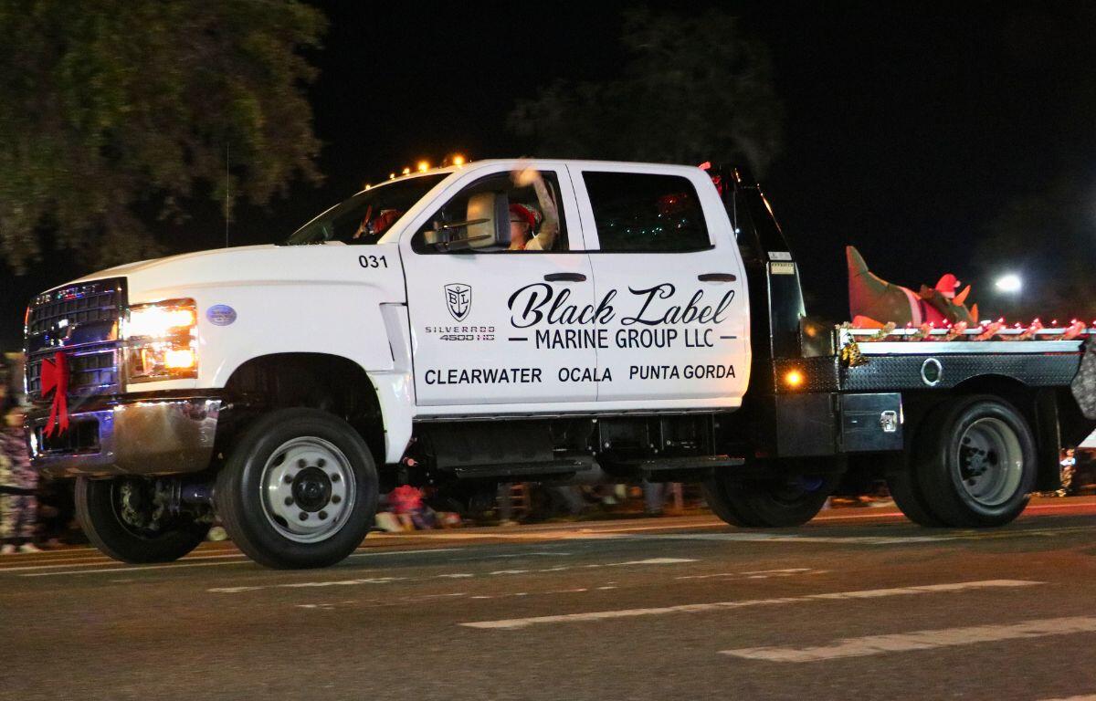 A white truck drives down a dimly lit road with Christmas decorations. The side of the truck reads, "Black Label Marine Group LLC."