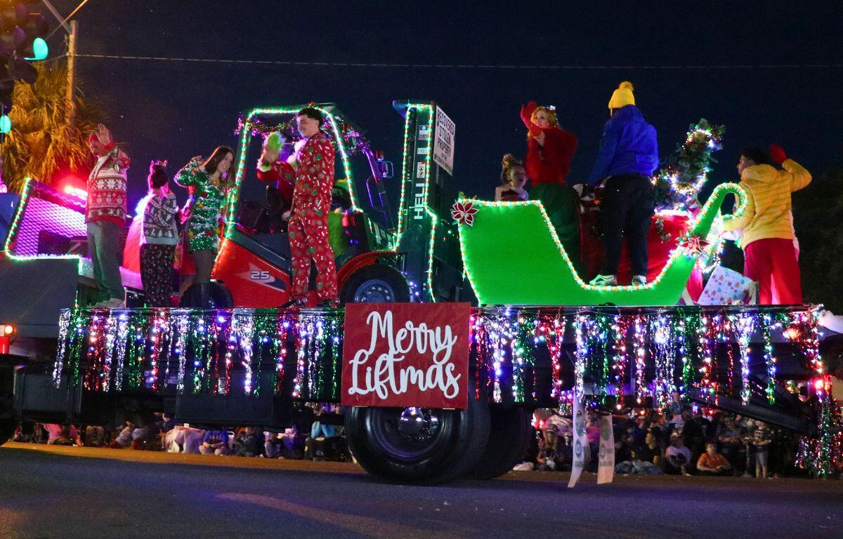 A truck bed decorated with Christmas lights and a sleigh with a small fork lift features multiple people in holiday attire.