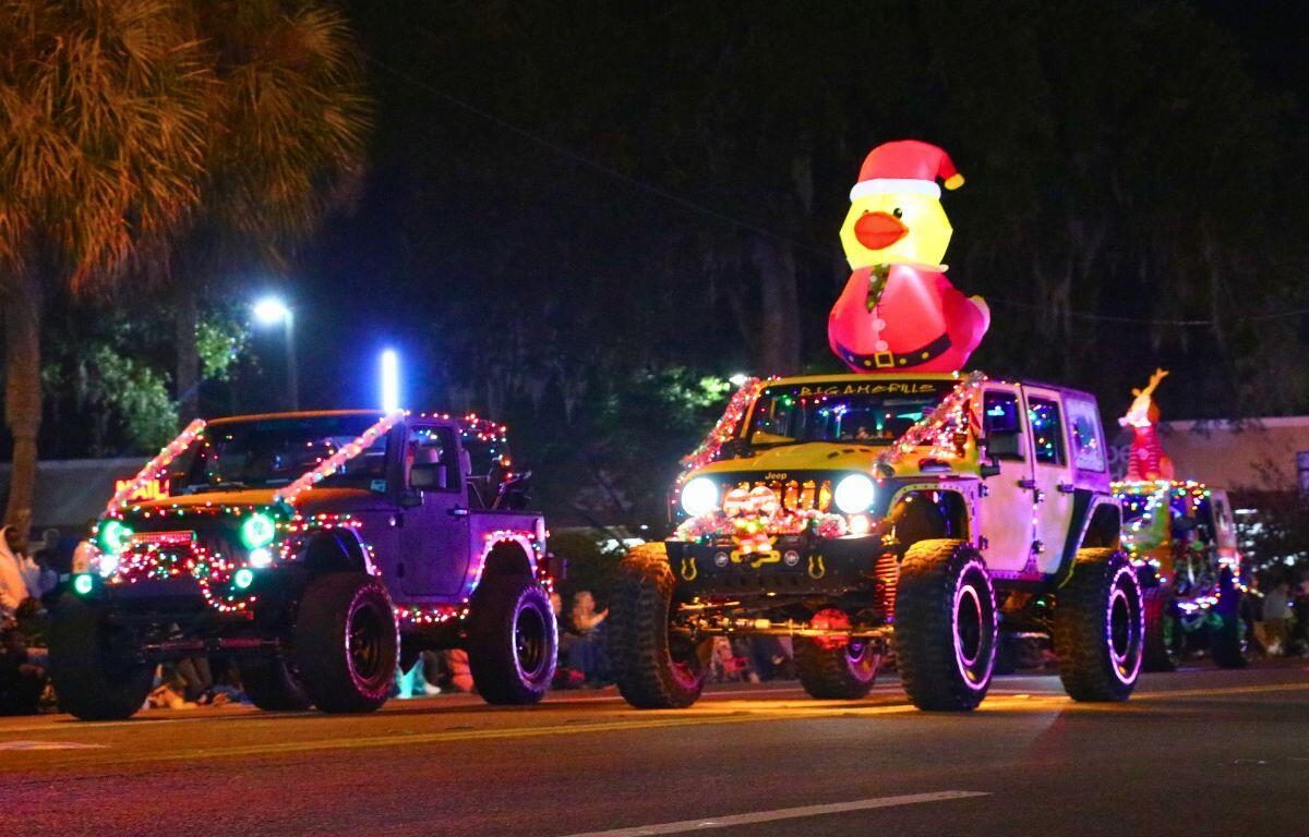 Jeeps decorated in Christmas lights and inflatables drive together on a dimly lit road.