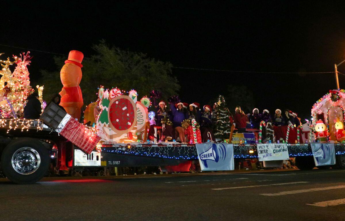 MCYFL Senior Cheer Champions stand together on a parade float with a gingerbread house and inflatable Christmas characters.