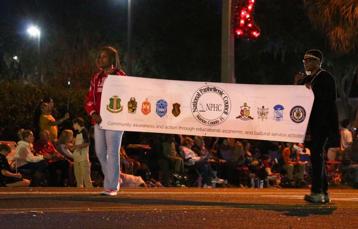 Two people hold a white banner that reads, "National Panhellenic Council. Marion County, FL." A crowd watches from behind.