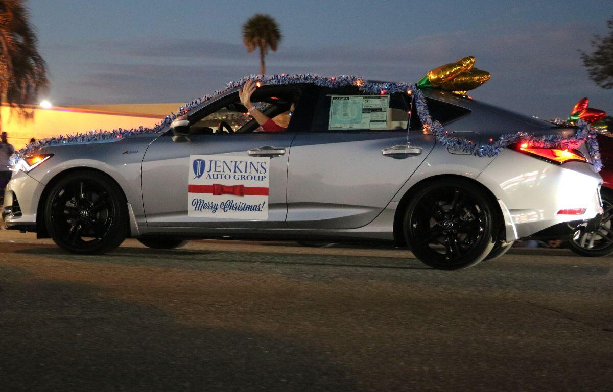 A gray car is decorated with Christmas lights with a sign reading, "Jenkins Auto Group. Merry Christmas."