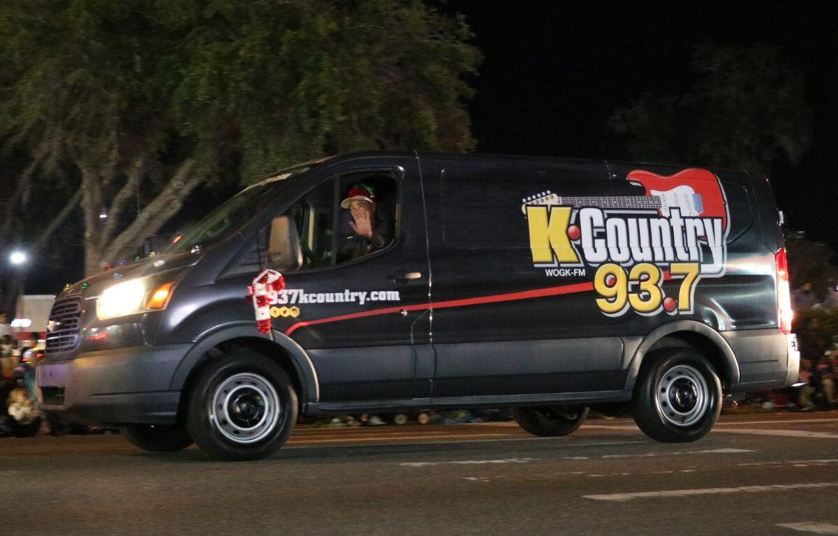 A black van with "K-Country 93.7," drives down a dark road with a decorative candy cane on it.