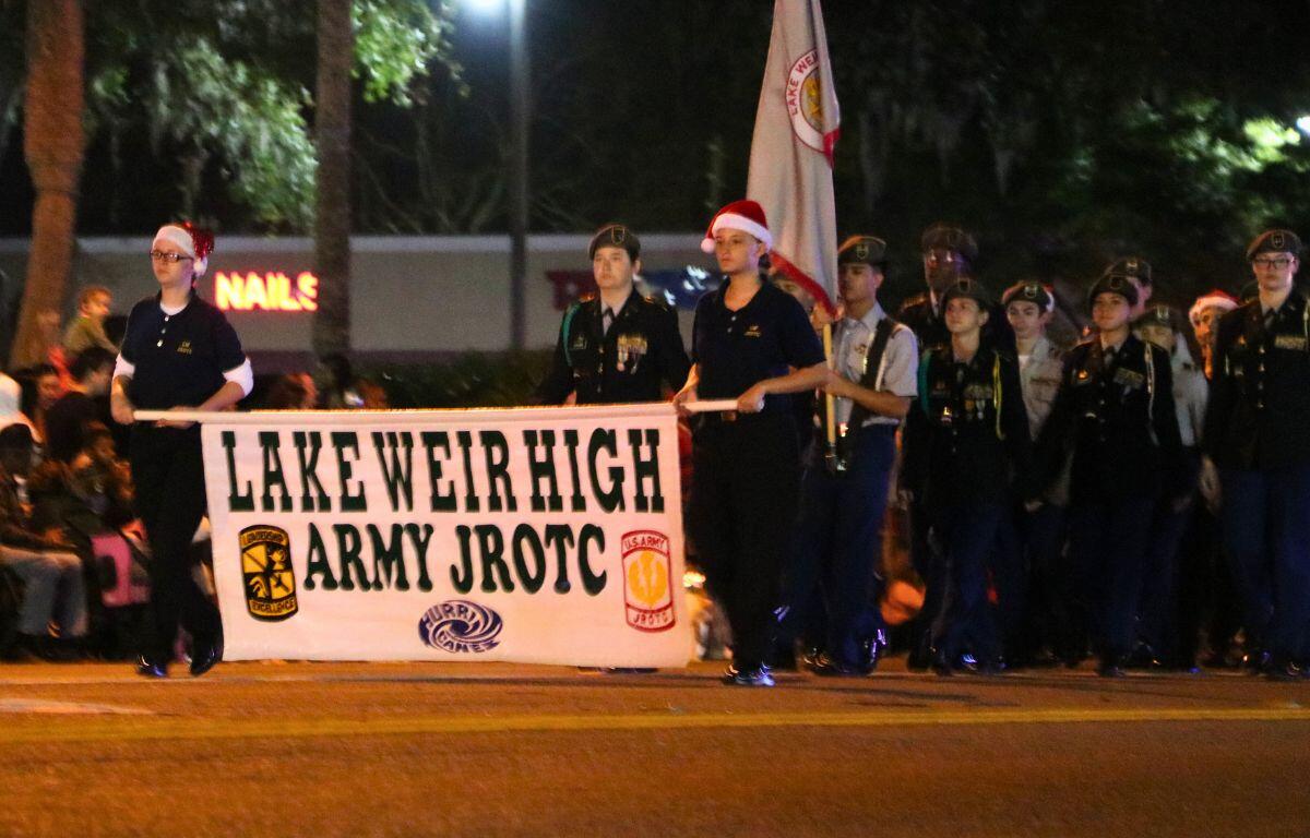 A group of students in JROTC uniforms march together holding banners and flags.