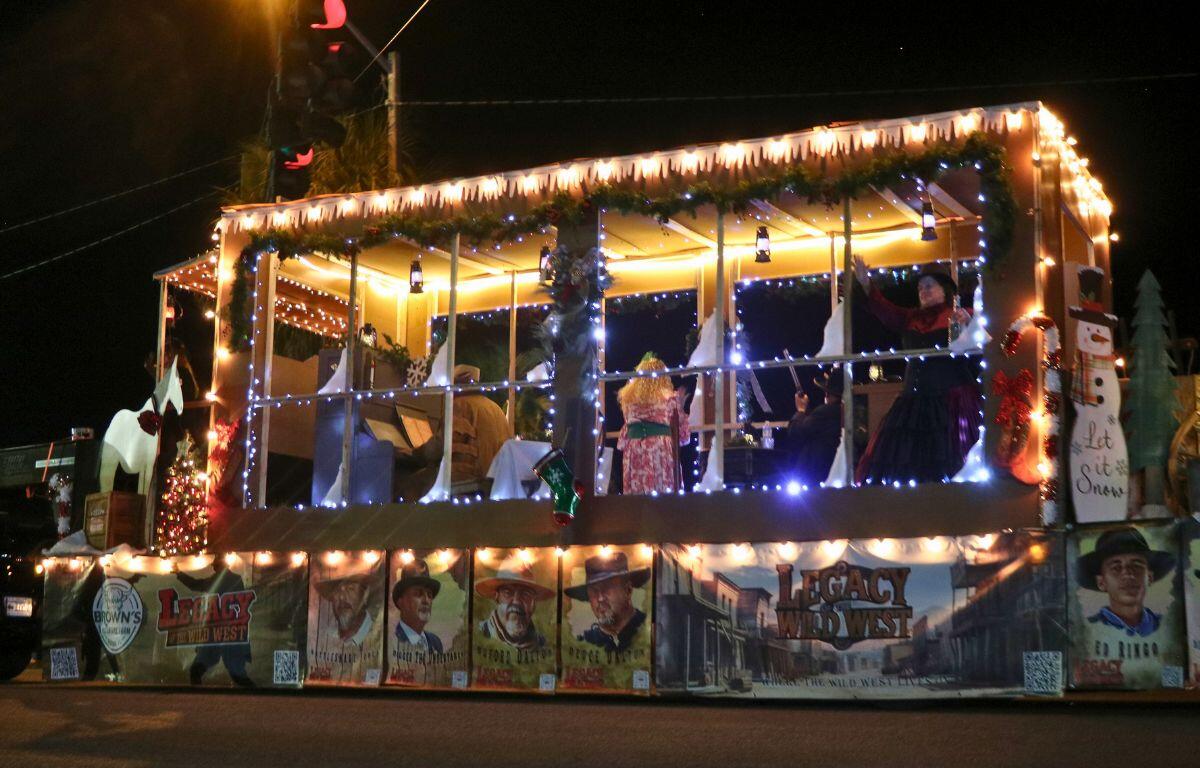 A parade float themed to the wild west features Christmas lights as it drives down a dark street.